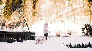 Durch die verschneite Winterlandschaft zieht ein Kind seinen Schlitten beim Familienhotel Alpura Retreat in Südtirol.