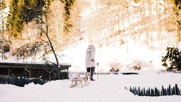 Durch die verschneite Winterlandschaft zieht ein Kind seinen Schlitten beim Familienhotel Alpura Retreat in Südtirol.