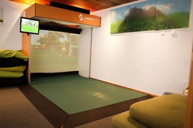 Indoor-Golf-Simulator im Familienhotel Landgut Furtherwirt mit großer Projektionsfläche, Abschlagmatte und alpiner Wandgestaltung für wetterunabhängigen Spielspaß.