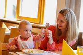 Ein Baby entdeckt gemeinsam mit seiner Mama mit viel Freude das erste eigene Besteck beim Essen im Familienhotel Ramsi