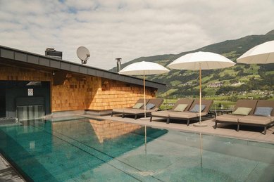 Eltern sitzen in der Sauna des Familienhotel Mia Alpina in Tirol mit Holzwänden, großem Fenster und winterlicher Bergkulisse.