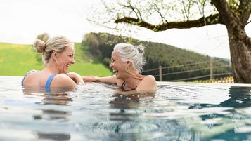 Mutter und Oma genießen gemeinsam den Moment im Außenpool eines Familienhotels mit Blick auf grüne Hügel.