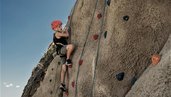 Ein Kind klettert beim Familienhotel Mia Alpina in Tirol gesichert an einer Felswand mit bunten Griffen.