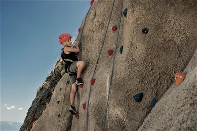Ein Kind klettert beim Familienhotel Mia Alpina in Tirol gesichert an einer Felswand mit bunten Griffen.