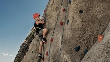Ein Kind klettert beim Familienhotel Mia Alpina in Tirol gesichert an einer Felswand mit bunten Griffen.