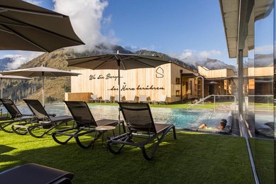 Außenpool mit Liegestühlen und Sonnenschirmen im Familienhotel Almfamilyhotel Scherer mit Blick auf die umliegende Berglandschaft.