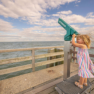 Mädchen blickt durch ein Fernrohr am Strand an der Ostsee.