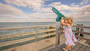 Mädchen blickt durch ein Fernrohr am Strand an der Ostsee.
