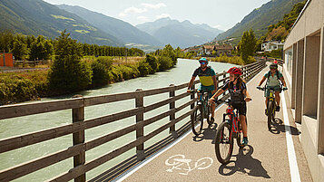 Teenager beim Fahrrad fahren mit der Familie. Die Strecke entlang am Fluss bietet eine tolle Aussicht auf die Berge in Südtirol im Sommer.