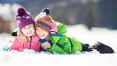 Ein Junge und ein Mädchen liegen lachend nebeneinander im Schnee.