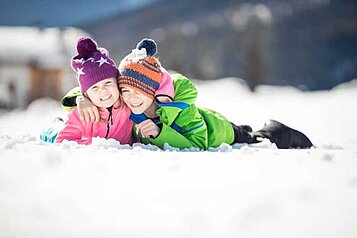 Ein Junge und ein Mädchen liegen lachend nebeneinander im Schnee.