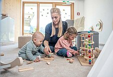 Mutter spielt im Babyzimmer mit ihrem Baby und Kleinkind mit den altersgerechten Spielsachen im Familienhotel Almfamilyhotel Scherer in Tirol.