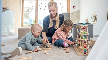 Mutter spielt im Babyzimmer mit ihrem Baby und Kleinkind mit den altersgerechten Spielsachen im Familienhotel Almfamilyhotel Scherer in Tirol.