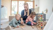 Mutter spielt im Babyzimmer mit ihrem Baby und Kleinkind mit den altersgerechten Spielsachen im Familienhotel Almfamilyhotel Scherer in Tirol.