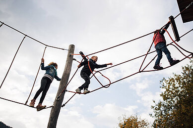 Drei Kinder klettern im Kletternetz auf dem Outdoor Spielplatz des Familienhotels Kirchheimerhof in Kärnten.