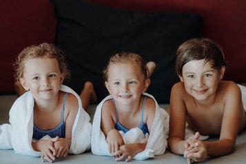 Drei Kinder im Familienhotel Oberkarteis entspannen fröhlich nach dem Schwimmen in Handtücher eingehüllt.