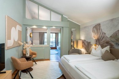 Modern eingerichtetes Familienzimmer mit Doppelbett, Sitzecke und Balkon im Familienhotel Post.