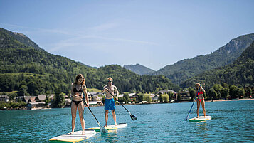 Salzburger Land Ausflugstipps: Familie fährt SUP auf dem Fuschlsee. Im Hintergrund ein herrliches Bergpanorama