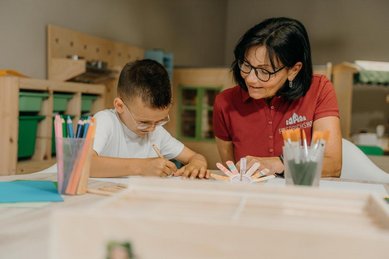 Ein Kind bastelt in der Kinderbetreuung des Familienhotel Friedrichshof in Bayern gemeinsam mit einer Betreuerin.