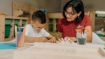 Ein Kind bastelt in der Kinderbetreuung des Familienhotel Friedrichshof in Bayern gemeinsam mit einer Betreuerin.