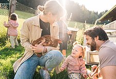 Eltern sind mit ihrem Kleinkind im Freilaufgehege der Hühner im Familienhotel Das Hopfgarten in Tirol.