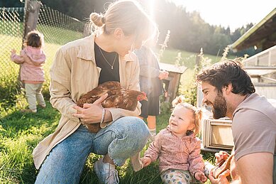 Eltern sind mit ihrem Kleinkind im Freilaufgehege der Hühner im Familienhotel Das Hopfgarten in Tirol.