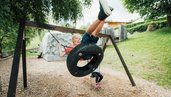 Junge schaukelt auf einer Reifen-Schaukel auf der Abenteuerwiese des Kinderhotels Sailer in Tirol.