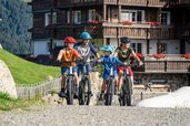 Familie mit Helmen beim Radfahren vor dem Familienhotel Allgäuer Berghof in alpiner Umgebung
