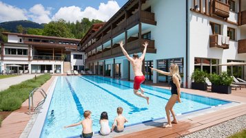Familie am Außenpool eines Alpenhotels, während ein Mann ins Wasser springt.