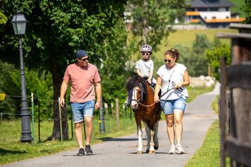 Kind reitet auf einem Pony, begleitet von zwei Erwachsenen bei einem Spaziergang im Familienhotel Furtherwirt.