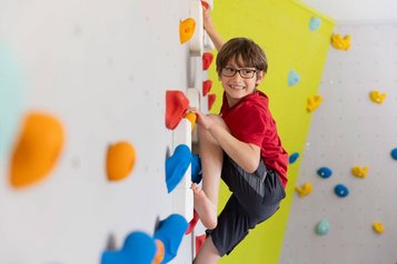 Junge klettert lachend an der bunten Indoor-Kletterwand im Familienhotel Ottonenhof.