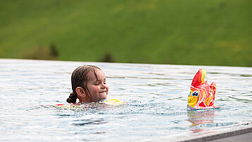 Ein Kind schwimmt im Outdoor-Pool des Familienhotels 