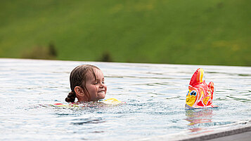 Ein Kind schwimmt im Outdoor-Pool des Familienhotels 