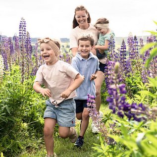 Kinder rennen fröhlich durch eine Blumenwiese, begleitet von ihrer Mutter.