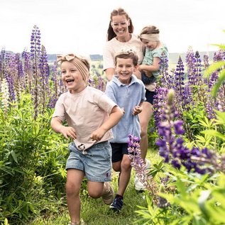 Kinder rennen fröhlich durch eine Blumenwiese, begleitet von ihrer Mutter.