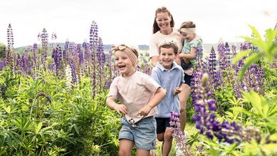 Kinder rennen fröhlich durch eine Blumenwiese, begleitet von ihrer Mutter.