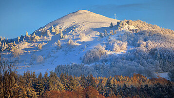 Rhön im Winter: Der schneebedeckte Gipfel "Pferdekopf" im Vordergrund ein herbstlicher Wald