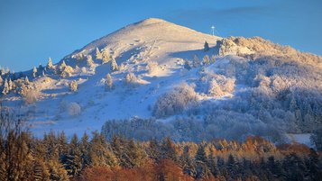 Rhön im Winter: Der schneebedeckte Gipfel "Pferdekopf" im Vordergrund ein herbstlicher Wald
