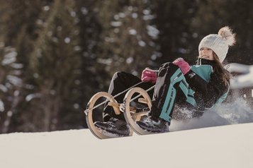 Ein Mädchen rodelt im Winter auf einer verschneiten Strecke beim Hotel Bella Vista in Südtirol.