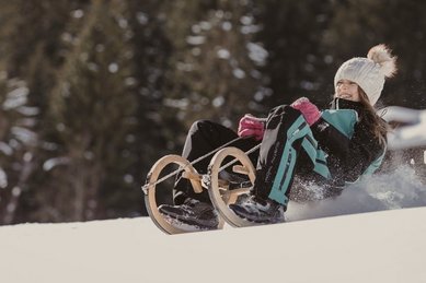 Ein Mädchen rodelt im Winter auf einer verschneiten Strecke beim Hotel Bella Vista in Südtirol.