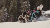 Ein Mädchen rodelt im Winter auf einer verschneiten Strecke beim Hotel Bella Vista in Südtirol.