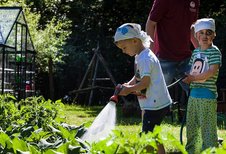 Zwei als Piraten verkleidete Kinder stehen im Gemüsegarten des Familienhotels Borchard's Rookhus an der Mecklenburgischen Seenplatte und gießen mit einem Gartenschlauch die Pflanzen.