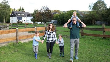 Eine Familie läuft über die Wiese und im Hintergrund sind die Pferde auf der Wiese im Familienhotel Monikas Ferienhof.