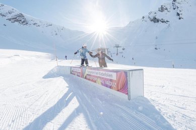Ein Kind fährt im Skigebiet nahe dem Familienhotel Gorfion in Liechtenstein auf Skiern über ein Hindernis im Schnee.