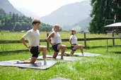 Drei Personen machen Yogaübungen auf Matten im Freien mit Blick auf die Berge beim Familienhotel Sonne Bezau.