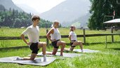 Drei Personen machen Yogaübungen auf Matten im Freien mit Blick auf die Berge beim Familienhotel Sonne Bezau.