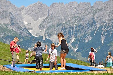 Kinder springen auf dem großen Trampolin, umgeben von beeindruckenden Bergpanorama im Familienurlaub in Tirol.