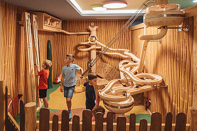 Kinder spielen im Spielbereich "Happy World" im Familienhotel Huber mit einer riesigen Murmelbahn aus Holz.