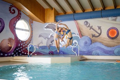 Zwei Mädchen springen lachend ins Hallenbad des Familienhotels Krone im Allgäu.