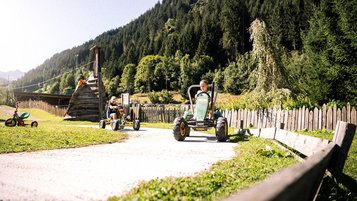Zwei Kinder fahren jeweils mit einem Riesen-Bobbycar auf einer Strecke am Alpura Retreat in Südtirol. 